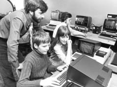 La imagen en blanco y negro muestra a dos escolares en clase de computación en los años setenta.