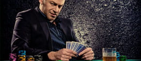 Un jugador de póker online con cartas en la mano y fichas a su derecha durante una partida mirando fijamente a la cámara.