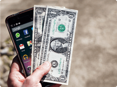 Teléfono móvil de pantalla grande sostenido por una mano junto con dos billetes de un dólar.